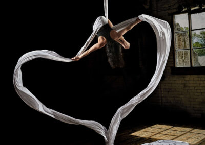 An aerial silk rope artist hanging upside down with 2 white silk ropes. her arms are spread out pushing the silks apart, they have formed the shape of a heart as they then gather on the floor. Image used by Sheffield food photgrapher Mark from Wildsmith.photography's