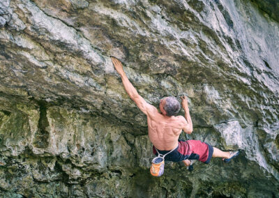 Steve McClure free climbing across a seam in a rockface. shirtless with the ripples of back muscles showing as he hangs on with just his fingers and toes. Image used by Sheffield food photgrapher Mark from Wildsmith.photography's
