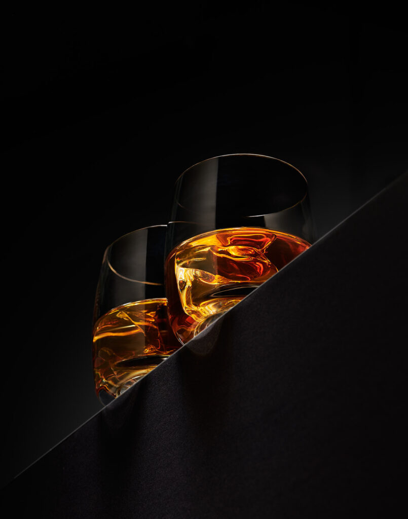 2 glasses of iced rum perched on the edge, the light through the ice looks like the drinks are full of flames and warmth. Shot by Sheffield food & drink photographer Mark Wildsmith. Photographed by Mark from Wildsmith Photography. Commercial food photographer and drink photographer based in London and Sheffield.