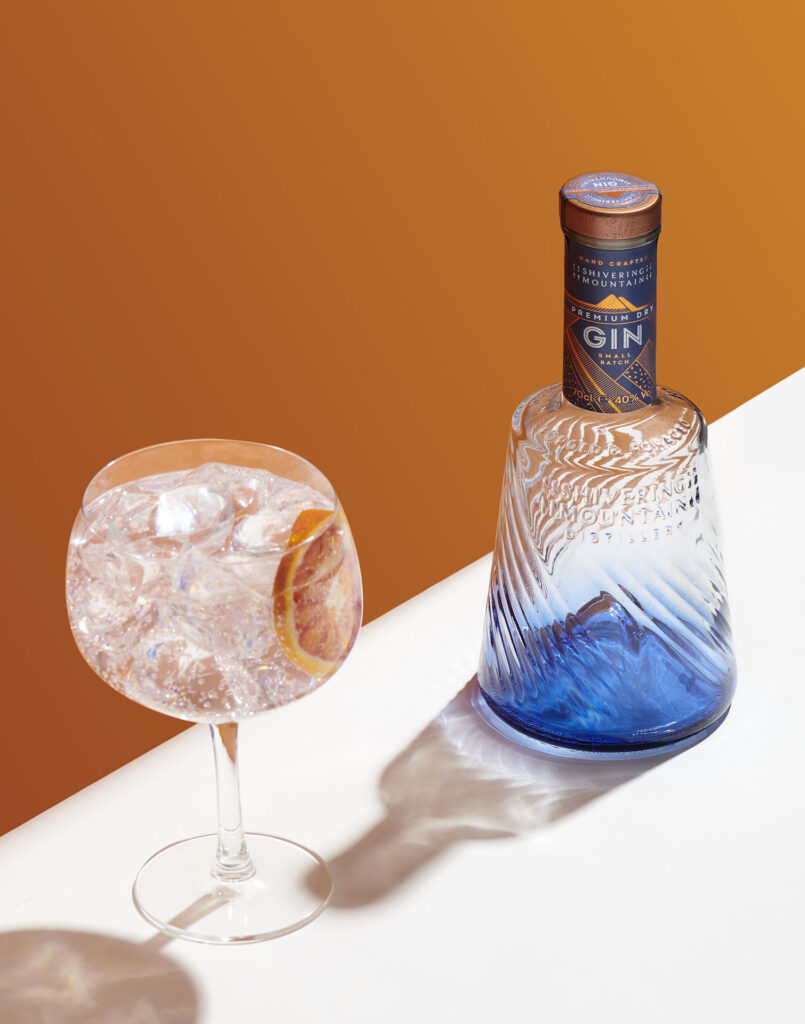 Shivering Mountain Gin and tonic, next to the bottle on a white background and orange wall behind. Sheffield's food and drink's photographer Mark Wildsmith. Photographed by Mark from Wildsmith Photography. Commercial food photographer and drink photographer based in London and Sheffield.