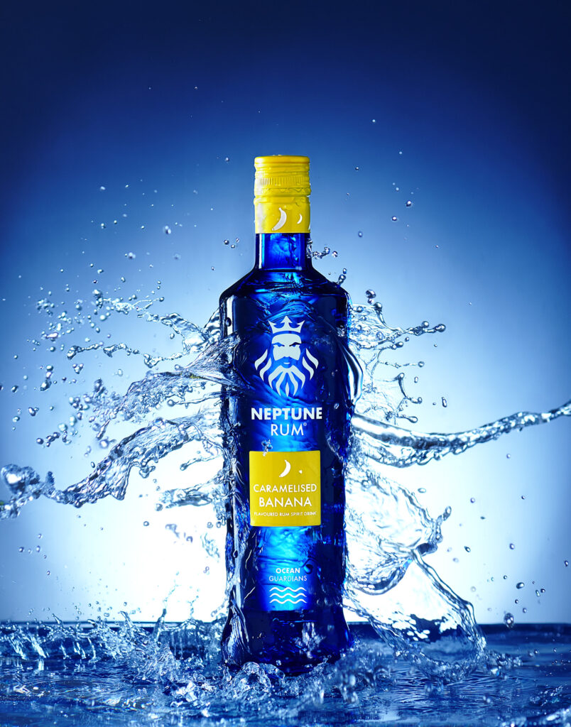 Caramelised Banana rum made by Neptune rum in Sheffield. Water crashing over the vivid blue bottle. Photographed by Mark Wildsmith from Wildsmith Photography in Sheffield