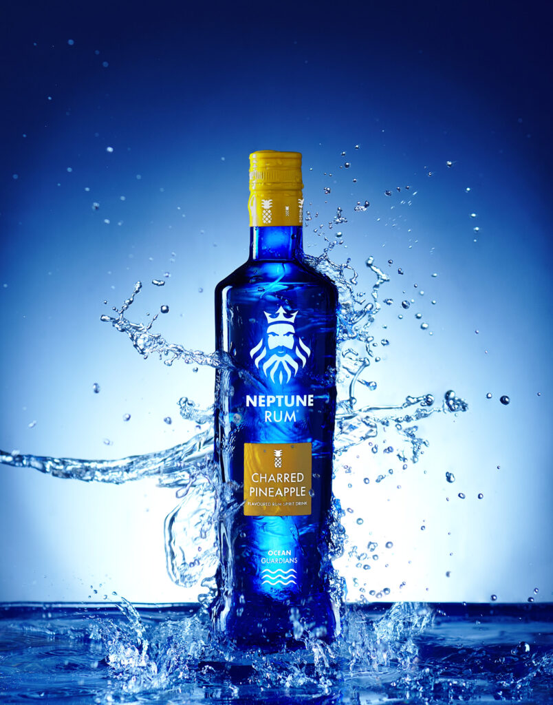 Charred pineapple rum made by Neptune rum in Sheffield. Water crashing over the vivid blue bottle. Photographed by Mark Wildsmith from Wildsmith Photography in Sheffield.