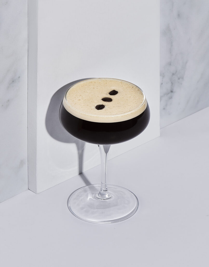 Espresso martini against a marble and white background, using hard light to form a shadow.